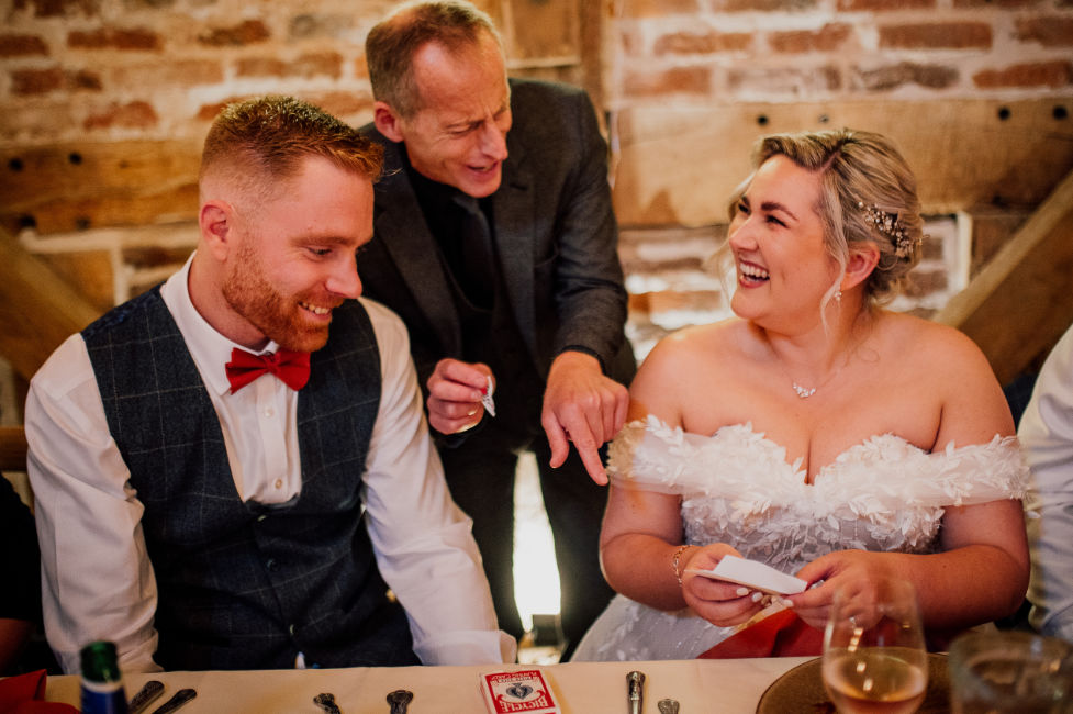 Barns and Yard Bride Groom Magicain Dearest Love Bride and groom being entertained by Brett Sirrell at the top table with an amazing card trick