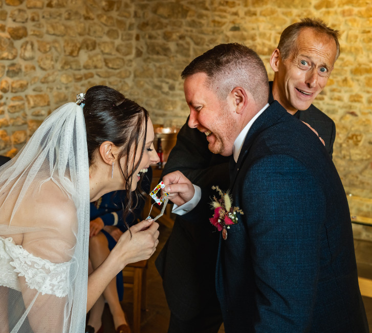 Sara and Andy cotwold wedding Bride and Groom share a laugh as they are entertained by Brett Sirrell Magic circle member at a Barn wedding venue