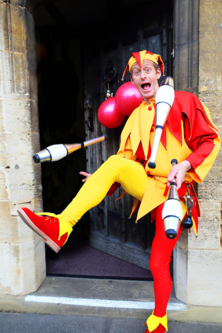 jester door 650 Red the Medieval jester being hired for an event as he juggles and entertains with magic and juggling before a party as guests arrive.
