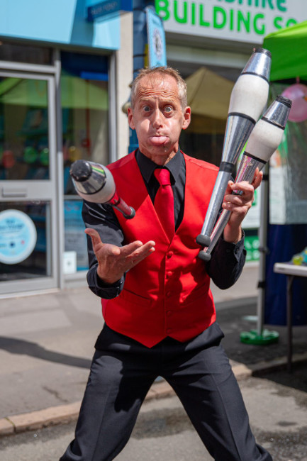street performer Brett Sirrell Juggling and entertaining as a street entertainer at a public event, juggling with juggling clubs in a market for a corporate event promotion